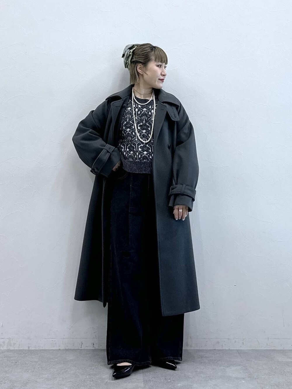 グレー系のステンカラーコート、ブラック系のニット/セーター、ブラック系のパンプスを着用したレディースの冬コーディネートの3枚目の写真