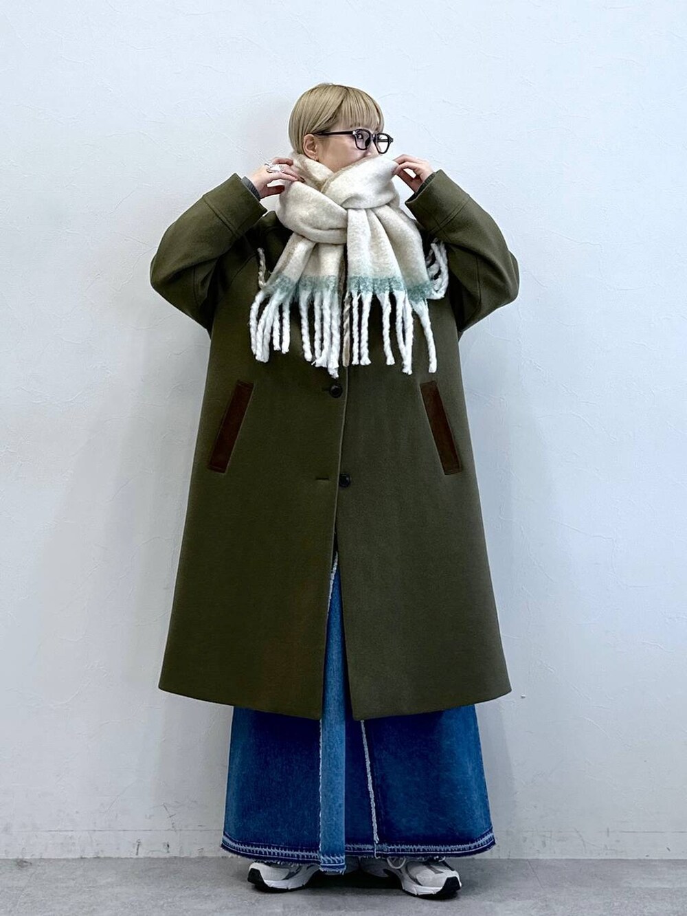 グリーン系のステンカラーコート、ブルー系のデニムスカート、ブラック系のサングラスを着用したレディースの冬コーディネートの2枚目の写真