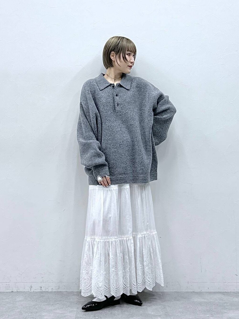 グレー系のポロシャツ、ホワイト系のスカート、ブラック系のパンプスを着用したレディースの冬コーディネートの2枚目の写真