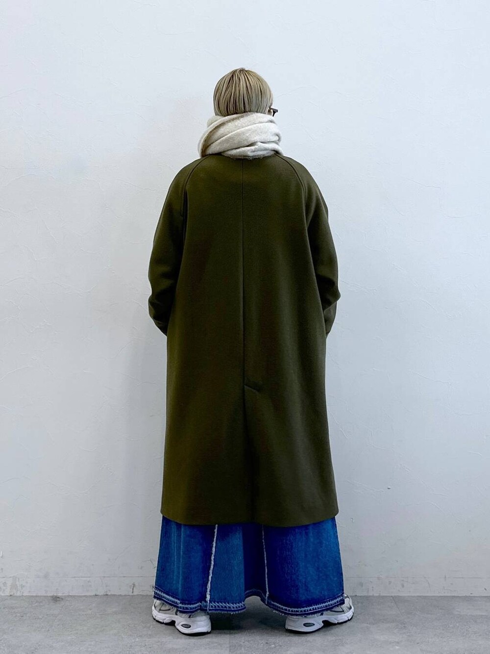 グリーン系のステンカラーコート、ブルー系のデニムスカート、ブラック系のサングラスを着用したレディースの冬コーディネートの4枚目の写真