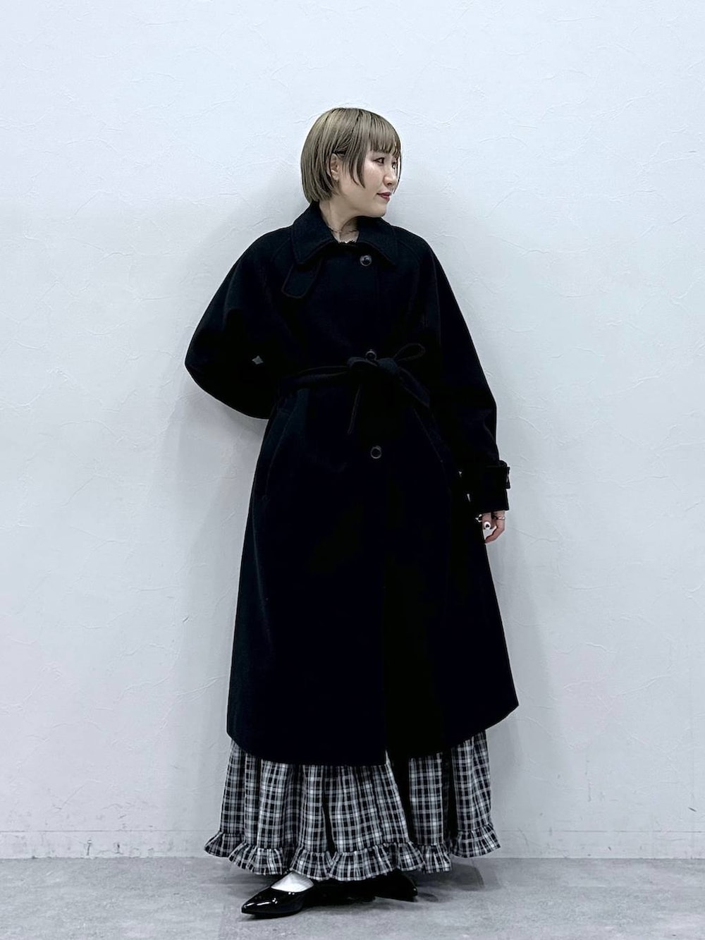 ブラック系のステンカラーコート、ブラック系のスカート、ブラック系のパンプスを着用したレディースの冬コーディネートの2枚目の写真