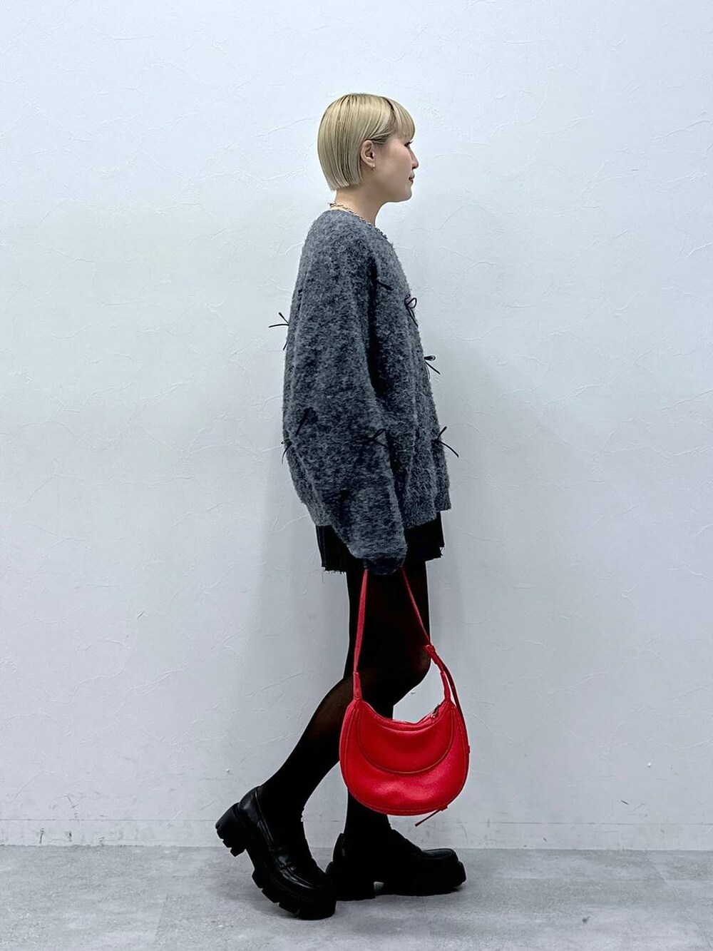 グレー系のスカート、レッド系のショルダーバッグ、グレー系のニット/セーターを着用したレディースの冬コーディネートの3枚目の写真