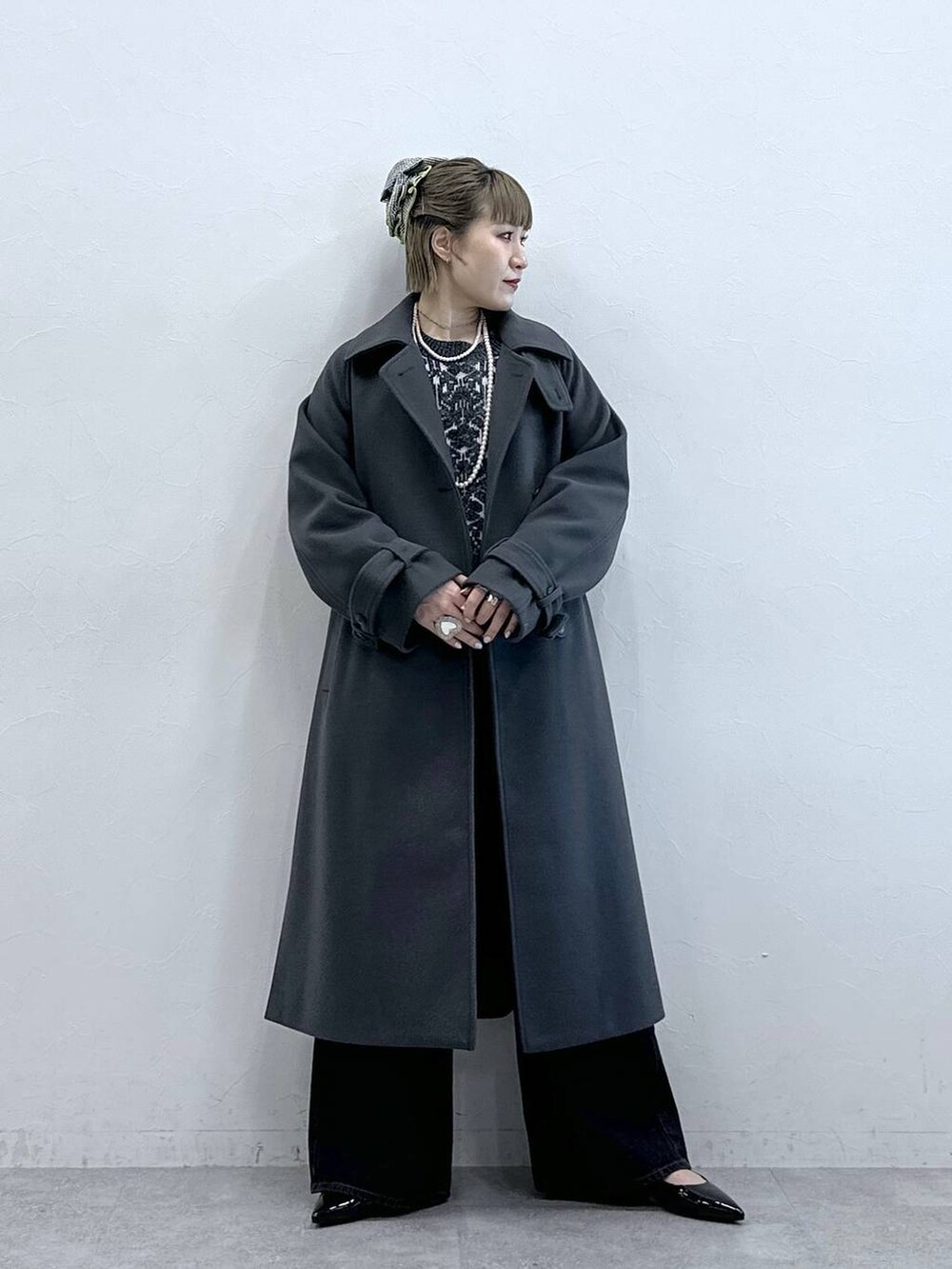 グレー系のステンカラーコート、ブラック系のニット/セーター、ブラック系のパンプスを着用したレディースの冬コーディネートの5枚目の写真