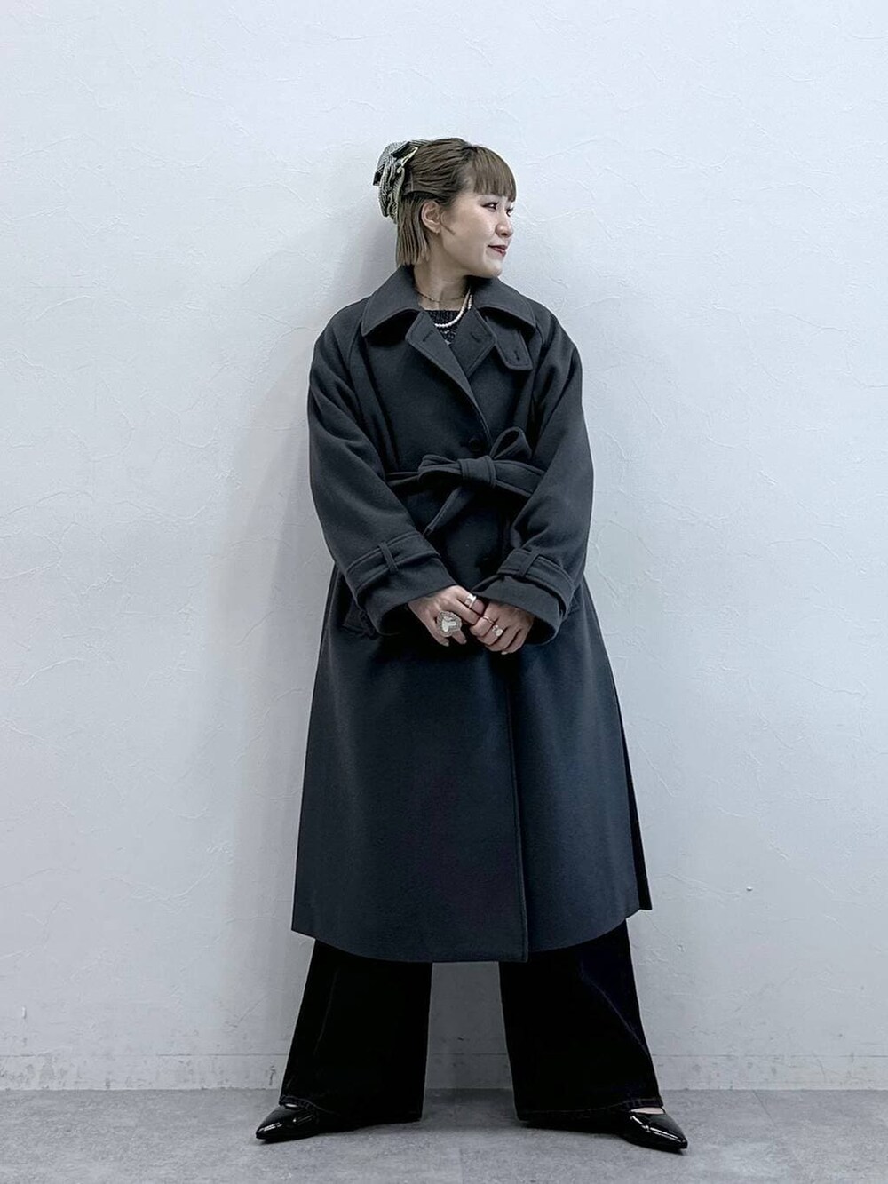 グレー系のステンカラーコート、ブラック系のニット/セーター、ブラック系のパンプスを着用したレディースの冬コーディネートの4枚目の写真