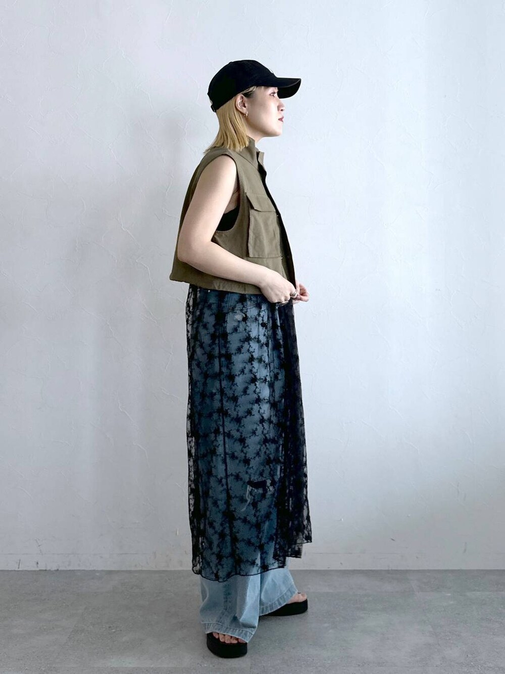 ブルー系のデニムパンツ、ブラック系のワンピース、グリーン系のベストを着用したレディースの夏コーディネートの2枚目の写真