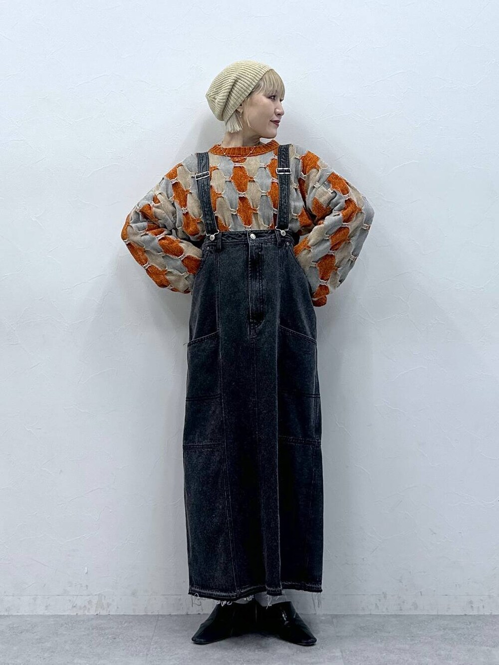 オレンジ系のニット/セーター、ブラック系のデニムスカート、ベージュ系のハンチング/ベレー帽を着用したレディースの秋コーディネートの2枚目の写真