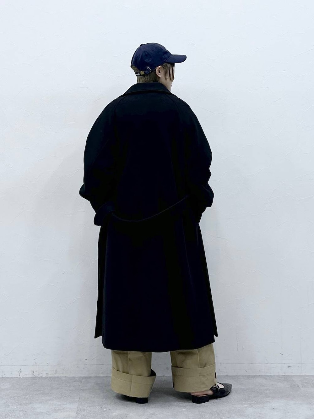 ブラック系のステンカラーコート、ブラウン系のニット/セーター、ベージュ系のチノパンツを着用したレディースの冬コーディネートの7枚目の写真