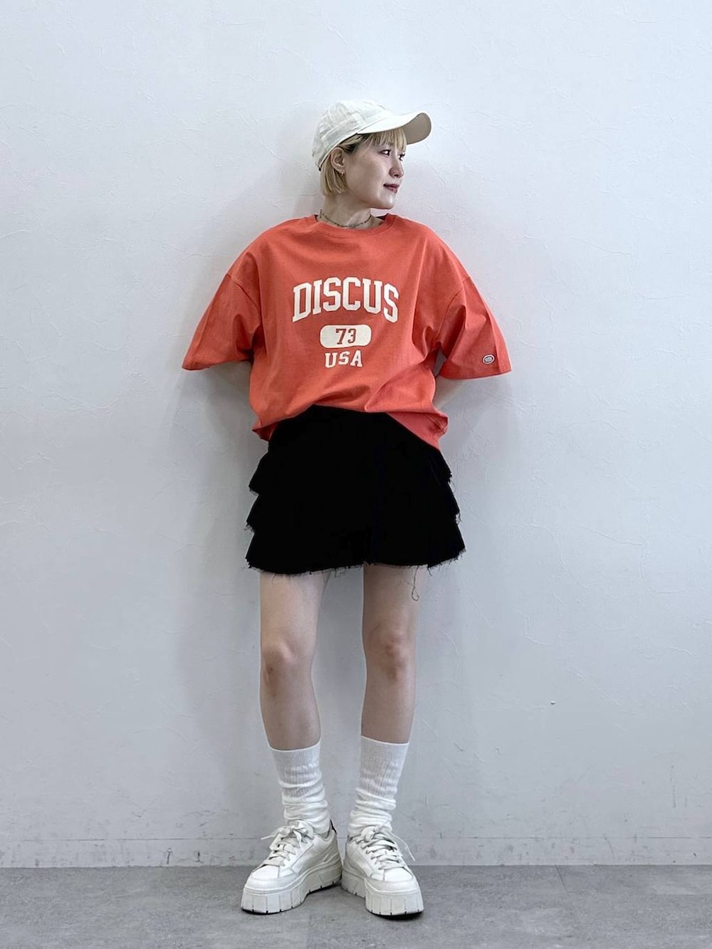 レッド系のTシャツ/カットソー、ブラック系のスカート、ホワイト系のキャップを着用したレディースの春コーディネートの3枚目の写真
