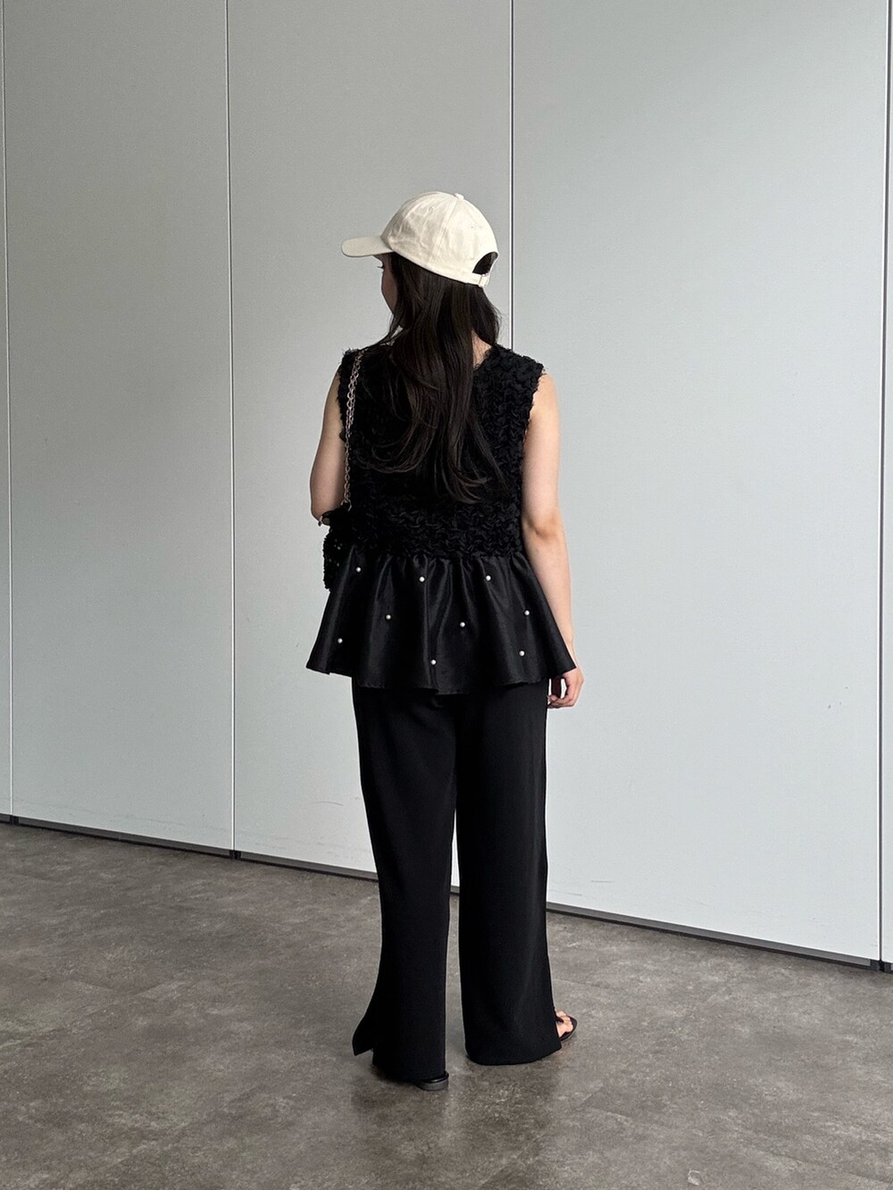 ブラック系のショルダーバッグ、ブラック系のベスト、ホワイト系のキャップを着用したレディースの夏コーディネートの2枚目の写真