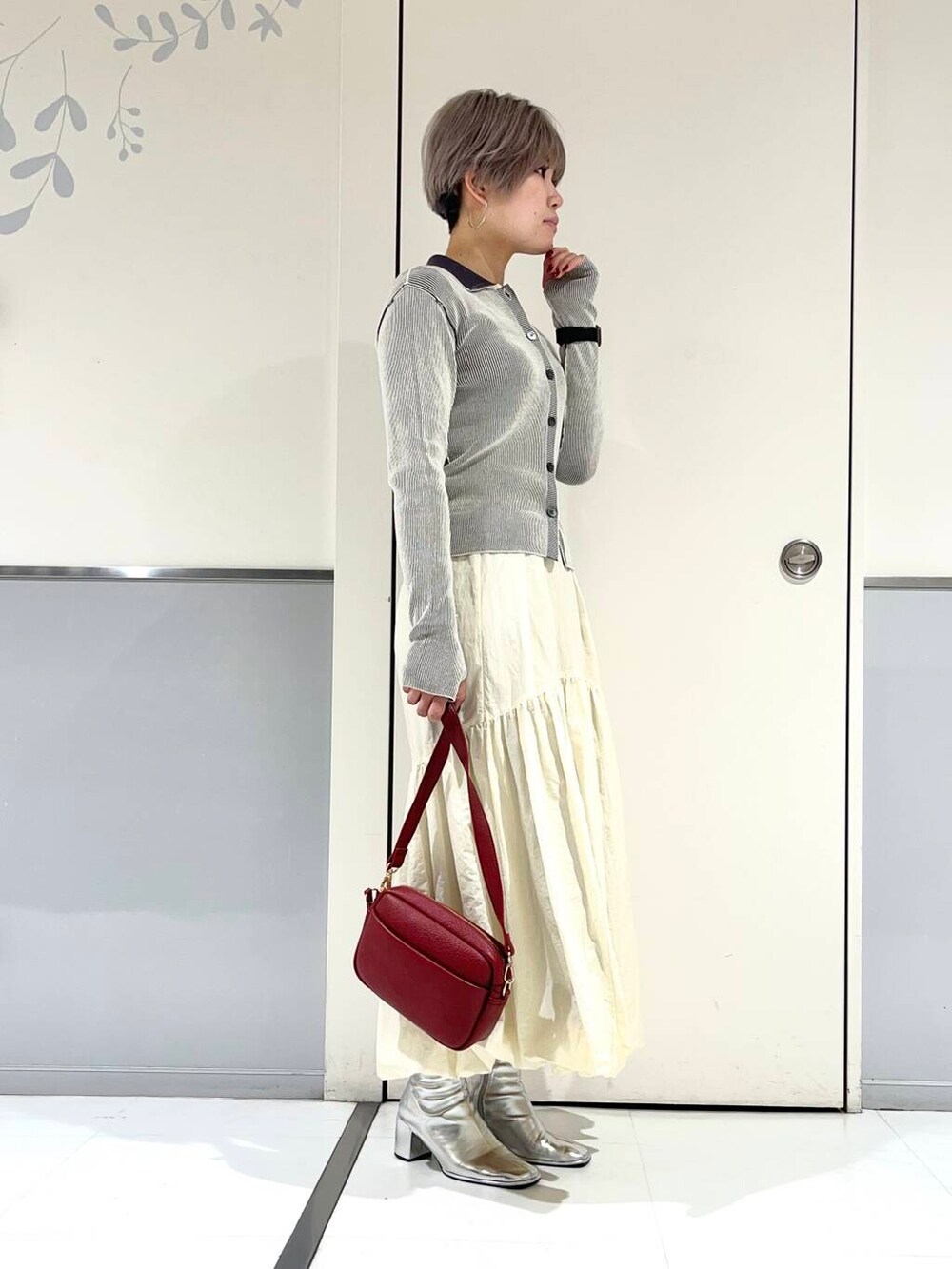 レッド系のショルダーバッグ、シルバー系のブーツ、ホワイト系のニット/セーターを着用したレディースの冬コーディネートの2枚目の写真