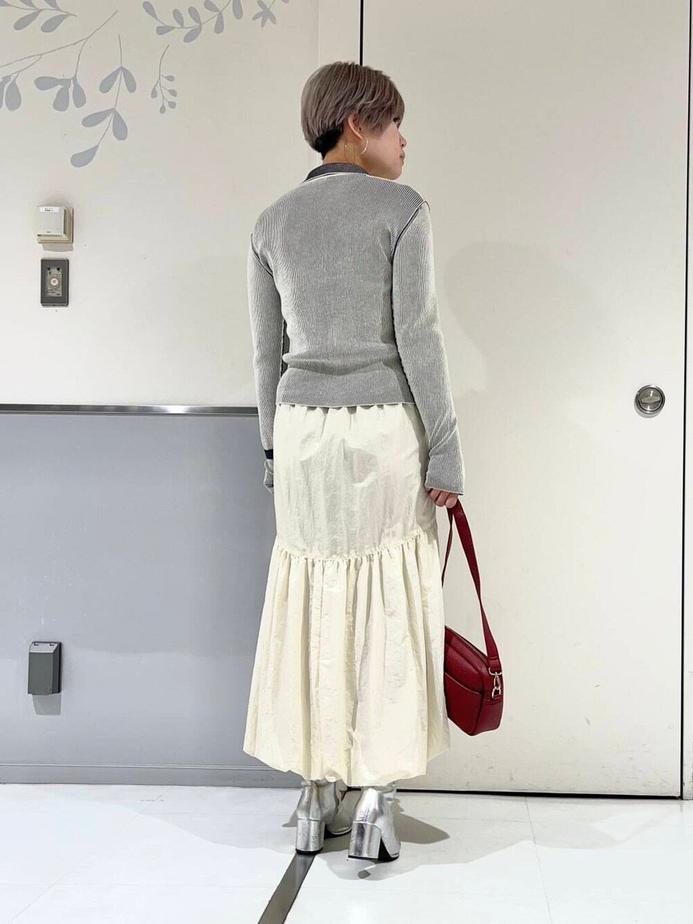 レッド系のショルダーバッグ、シルバー系のブーツ、ホワイト系のニット/セーターを着用したレディースの冬コーディネートの3枚目の写真