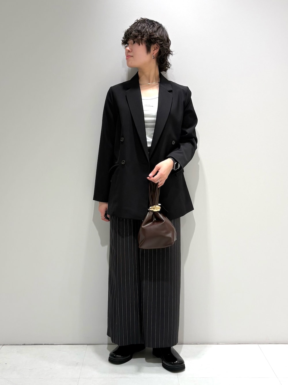 ブラック系のテーラードジャケット、グレー系のスカート、ブラック系のサンダルを着用したレディースの春コーディネートの2枚目の写真