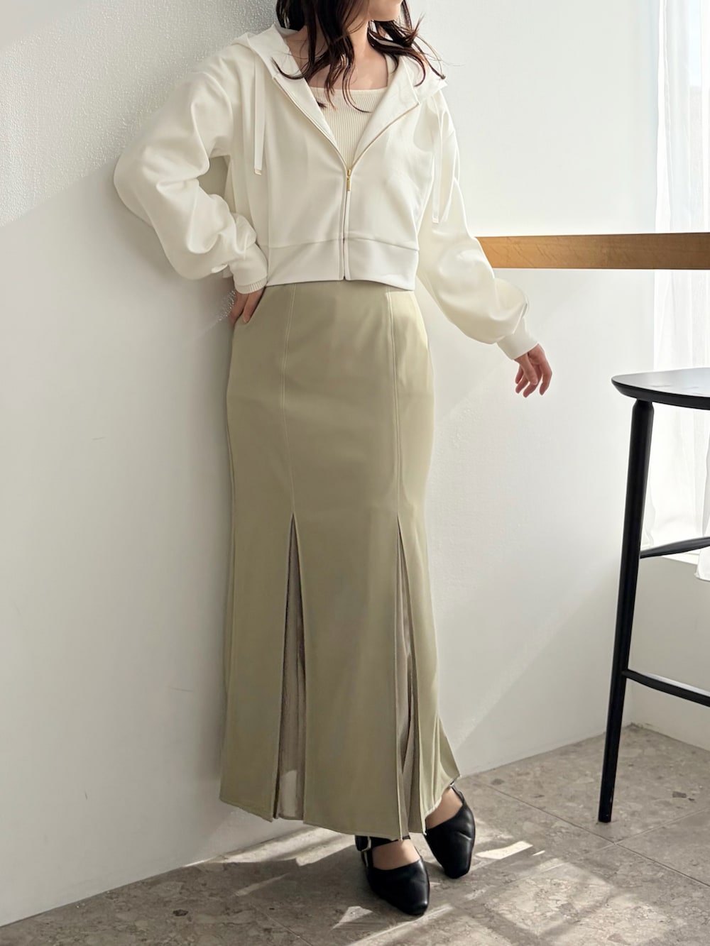 グリーン系のスカート、ブラック系のパンプス、ホワイト系のパーカーを着用したレディースの春コーディネートの2枚目の写真