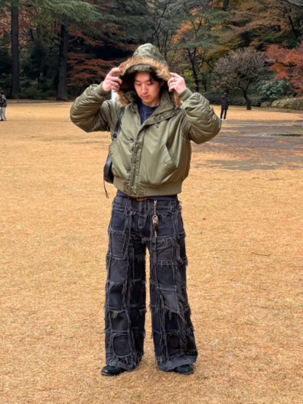 グリーン系のミリタリージャケット、ブラック系のデニムパンツ、ブラック系のショルダーバッグを着用したメンズの春コーディネートの2枚目の写真