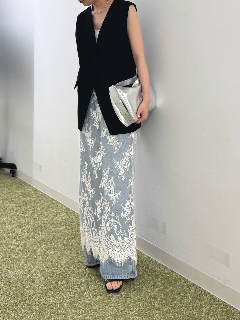 ブラック系のベスト、シルバー系のショルダーバッグ、ホワイト系のスカートを着用したレディースの春コーディネートの2枚目の写真