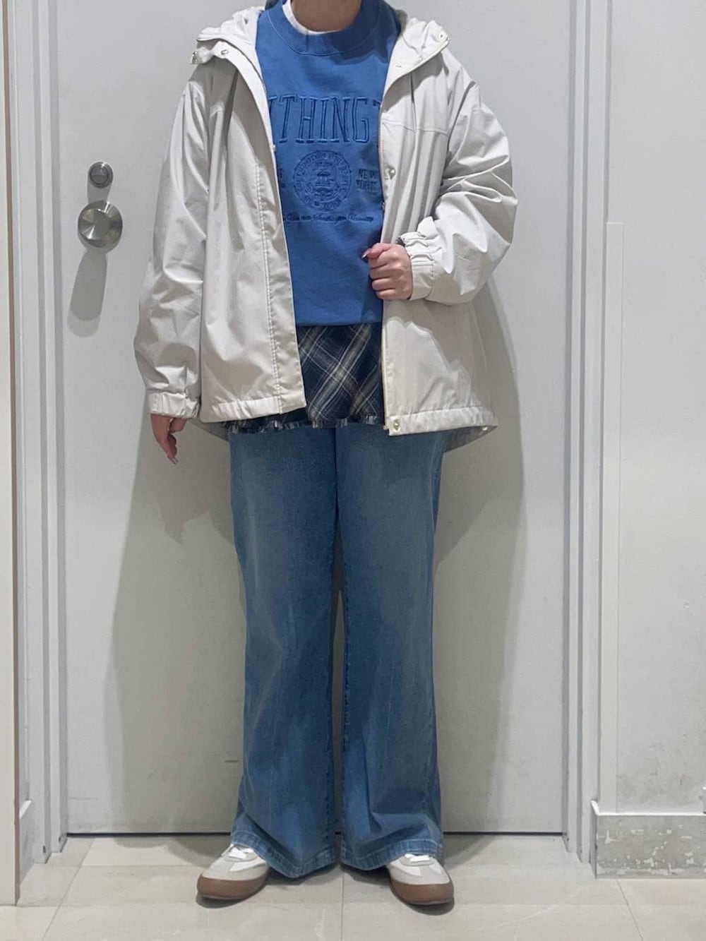 ホワイト系のスニーカー、ブルー系のデニムパンツ、ベージュ系のマウンテンパーカーを着用したレディースの春コーディネートの2枚目の写真