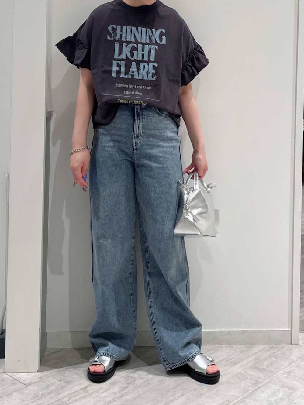 シルバー系のショルダーバッグ、ブルー系のデニムパンツ、シルバー系のサンダルを着用したレディースの春コーディネートの2枚目の写真