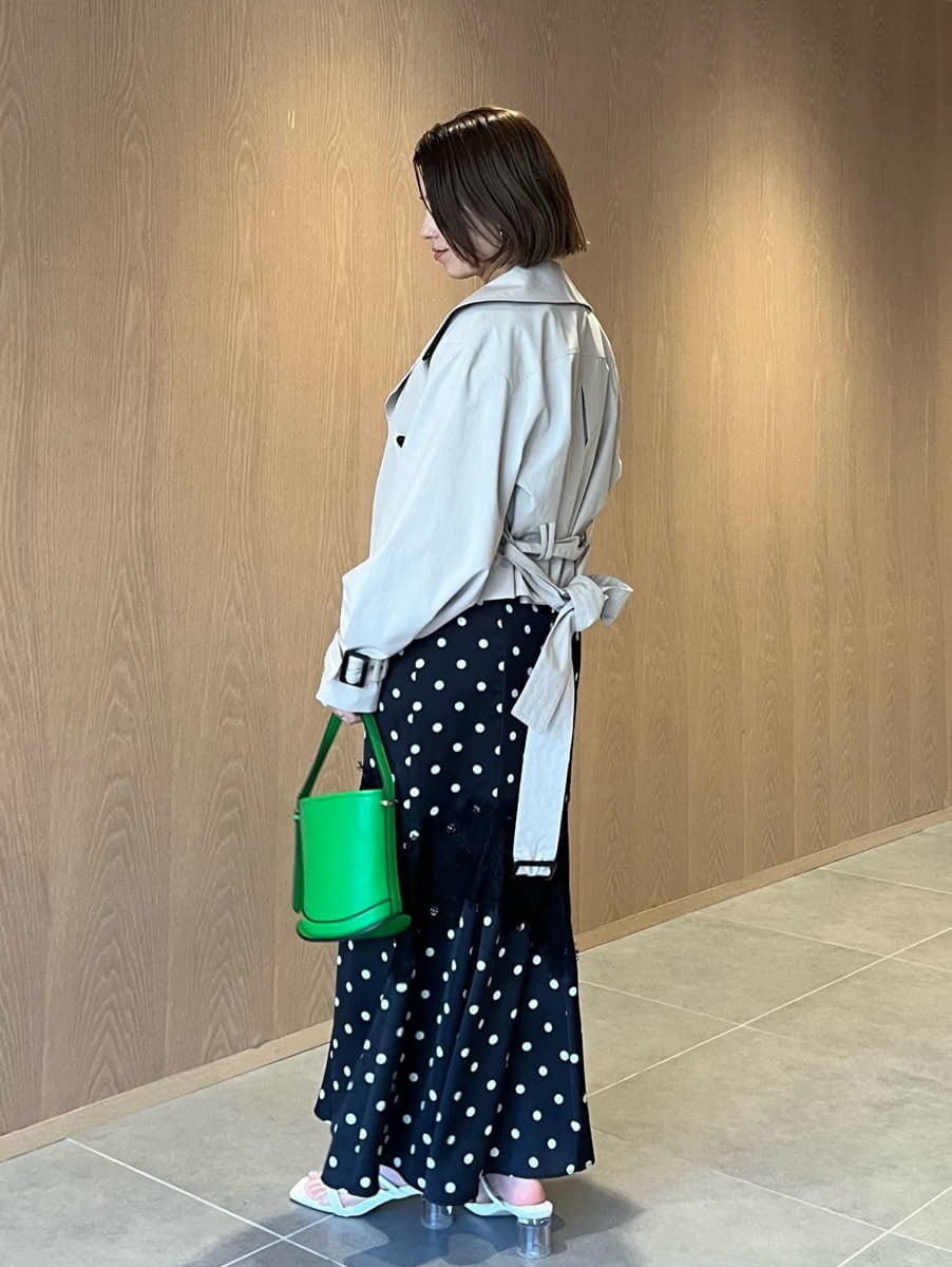 ベージュ系のトレンチコート、ブラック系のワンピース、グリーン系のハンドバッグを着用したレディースの春コーディネートの2枚目の写真