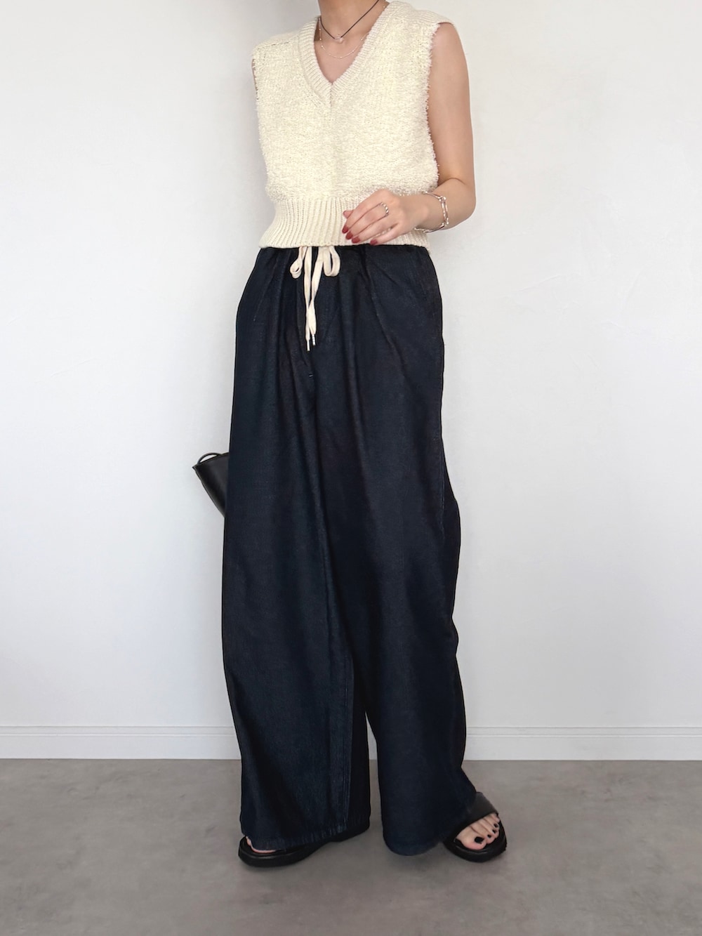 ブルー系のデニムパンツ、ホワイト系のベスト、ブラック系のトートバッグを着用したレディースの春コーディネートの2枚目の写真