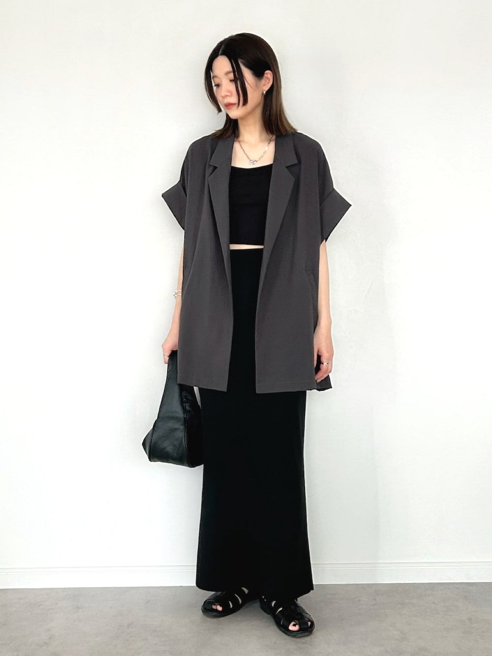 グレー系のテーラードジャケット、ブラック系のスカート、ブラック系のハンドバッグを着用したレディースの夏コーディネートの2枚目の写真