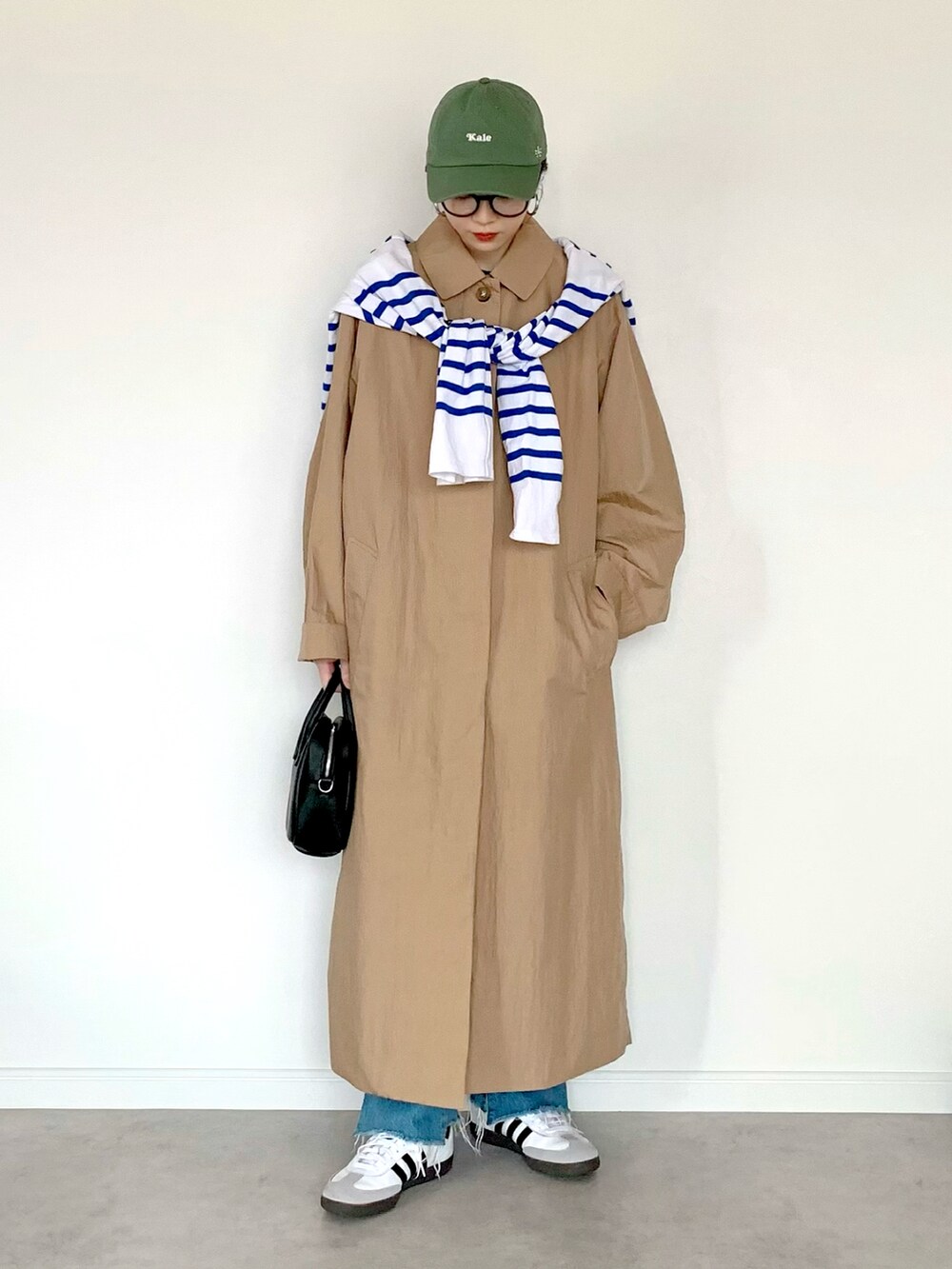 ブラック系のハンドバッグ、ベージュ系のステンカラーコート、ホワイト系のTシャツ/カットソーを着用したレディースの春コーディネートの2枚目の写真