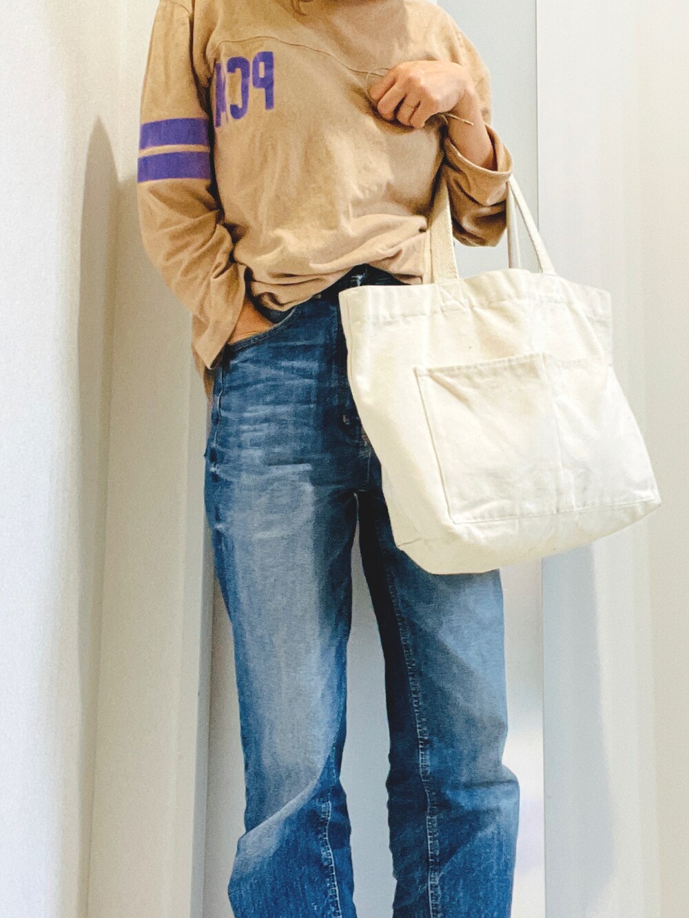 ブルー系のデニムパンツ、ブラック系のスニーカー、ベージュ系のTシャツ/カットソーを着用したレディースの秋コーディネートの2枚目の写真