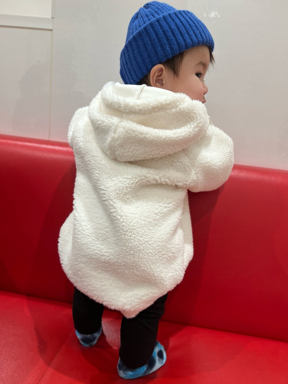 ブルー系の帽子、ホワイト系のスタイ/よだれかけ、ブルー系のベビーシューズ/ベビーソックスを着用したキッズの冬コーディネートの2枚目の写真