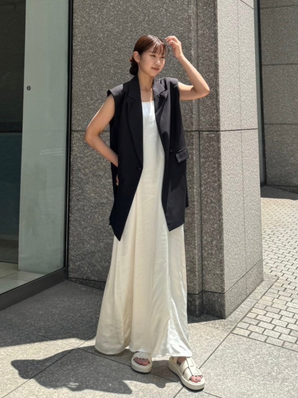 ホワイト系のワンピース、ブラック系のベスト、ホワイト系のサンダルを着用したレディースの夏コーディネートの2枚目の写真