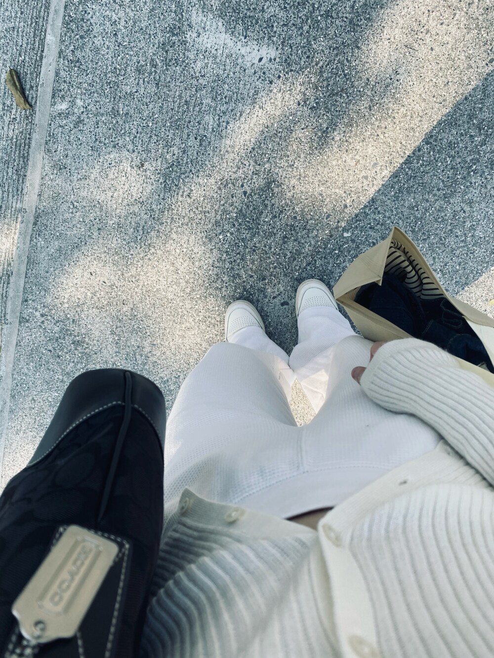 ブラック系のバッグ、ホワイト系のニット/セーター、ホワイト系のチノパンツを着用したレディースの春コーディネートの2枚目の写真