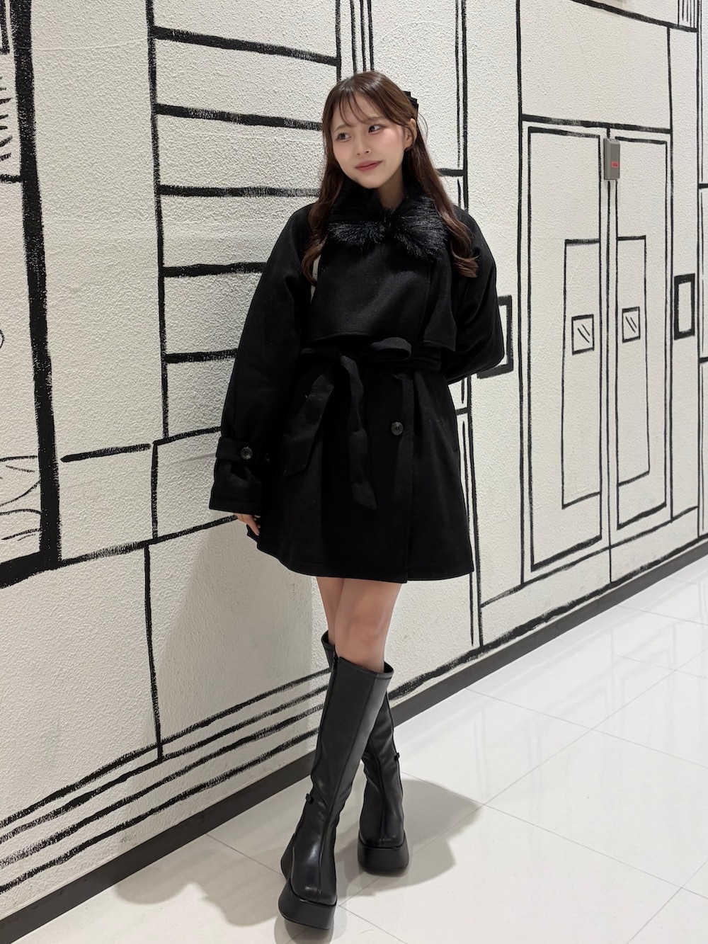 ブラック系のステンカラーコート、ブラック系のブーツを着用したレディースの秋コーディネートの3枚目の写真