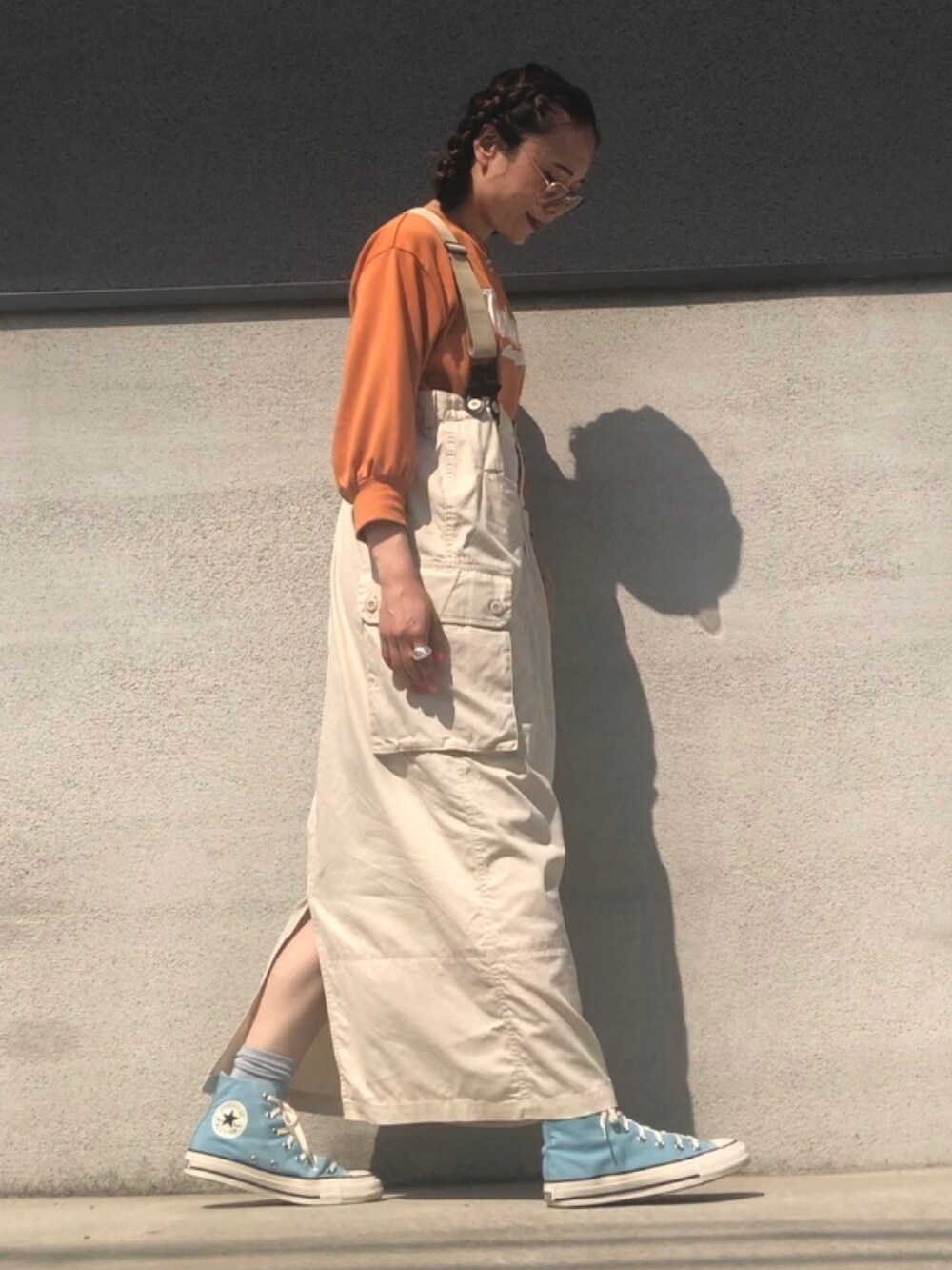 オレンジ系のTシャツ/カットソー、ベージュ系のジャンパースカート、ブルー系のスニーカーを着用したレディースの春コーディネートの2枚目の写真