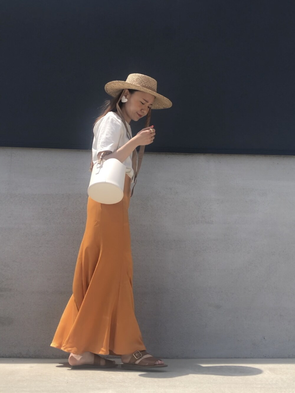 オレンジ系のスカート、ホワイト系のTシャツ/カットソー、ベージュ系のハットを着用したレディースの春コーディネートの3枚目の写真