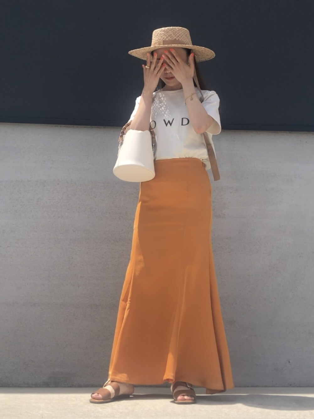 オレンジ系のスカート、ホワイト系のTシャツ/カットソー、ベージュ系のハットを着用したレディースの春コーディネートの2枚目の写真