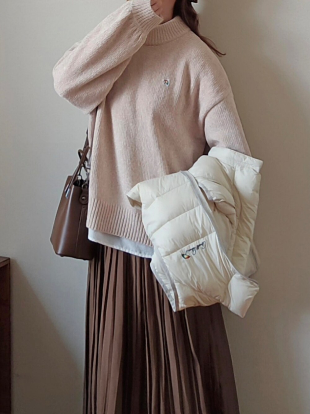 ベージュ系のニット/セーター、ホワイト系のダウンベスト、ブラウン系のハンドバッグを着用したレディースの冬コーディネートの3枚目の写真