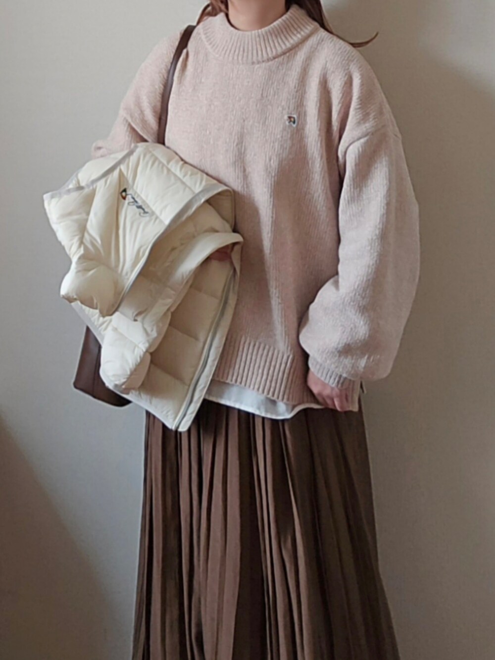 ベージュ系のニット/セーター、ホワイト系のダウンベスト、ブラウン系のハンドバッグを着用したレディースの冬コーディネートの4枚目の写真