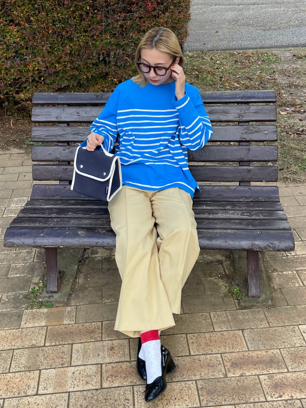 イエロー系のパンツ、ブルー系のショルダーバッグ、ブラック系のレインシューズを着用したレディースの秋コーディネートの2枚目の写真