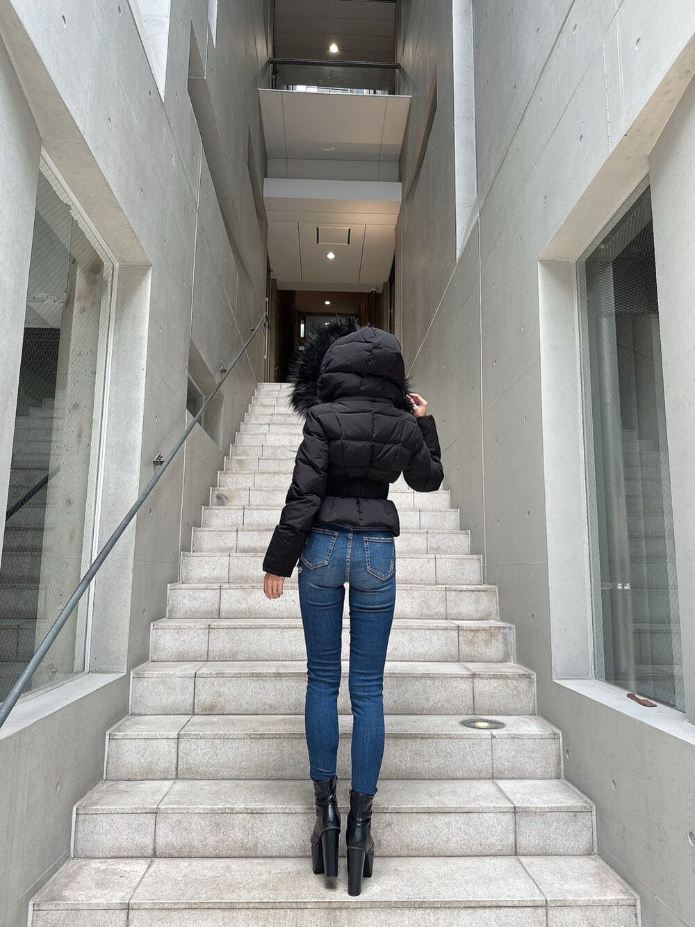 ブラック系のダウンジャケット/コート、ブラック系のブーツ、ブルー系のデニムパンツを着用したレディースの秋コーディネートの4枚目の写真