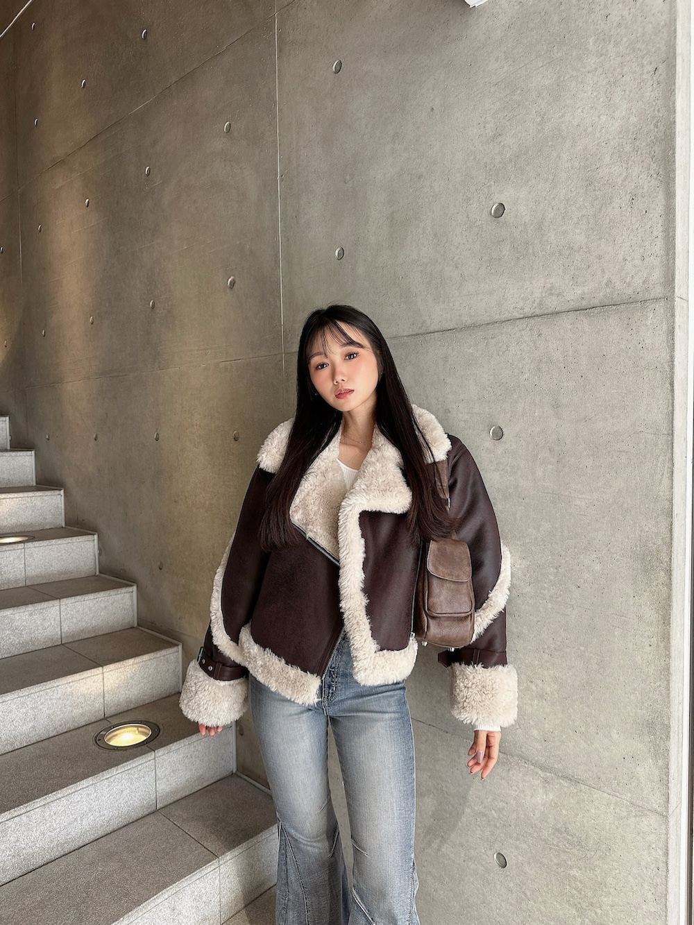 ブラウン系のムートンコート、ブルー系のデニムパンツ、ホワイト系のパンプスを着用したレディースの秋コーディネートの2枚目の写真