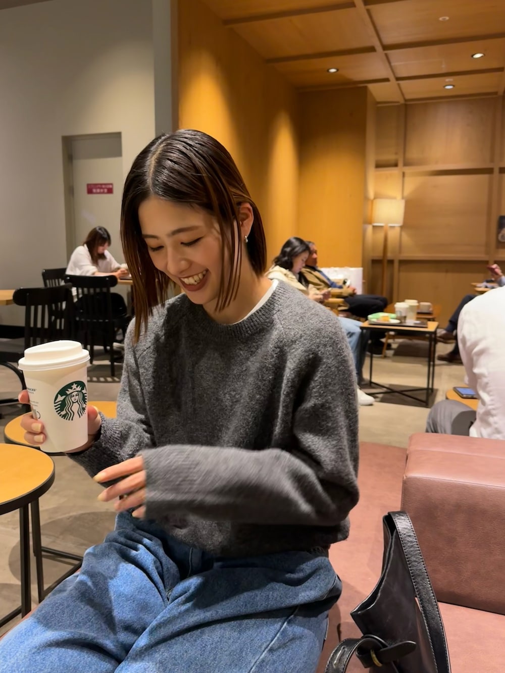 グレー系のニット/セーター、ブルー系のデニムパンツ、ブラック系のショルダーバッグを着用したレディースの秋コーディネートの3枚目の写真