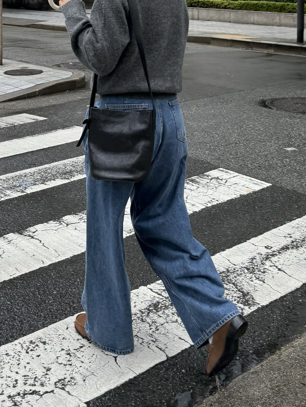 グレー系のニット/セーター、ブルー系のデニムパンツ、ブラック系のショルダーバッグを着用したレディースの秋コーディネートの2枚目の写真