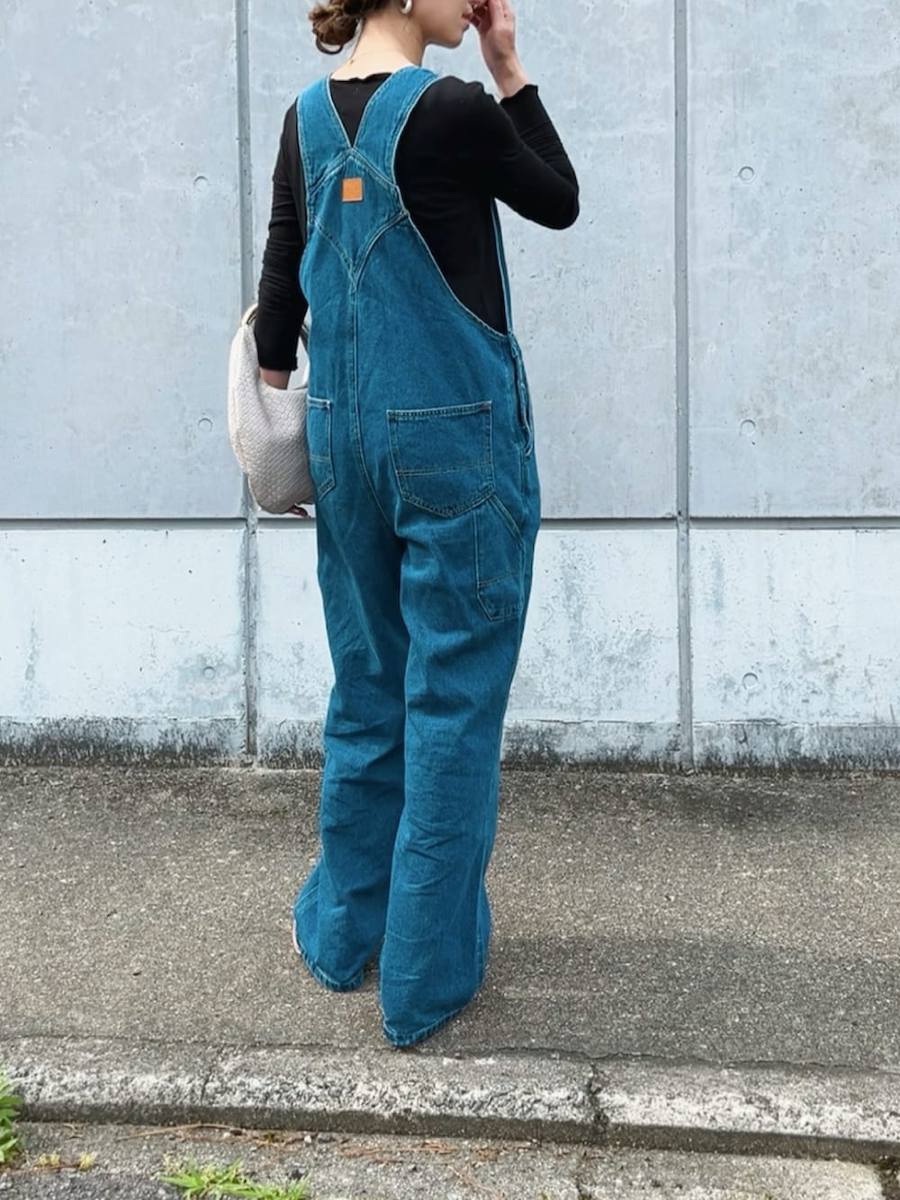 ブルー系のサロペット/オーバーオール、ブラック系のTシャツ/カットソー、ベージュ系のサンダルを着用したレディースの春コーディネートの3枚目の写真