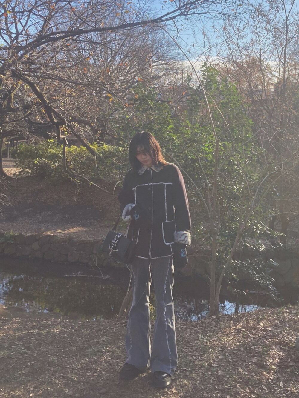 ブラック系のムートンコート、ブラック系のハンドバッグ、グレー系のデニムパンツを着用したメンズの冬コーディネートの2枚目の写真