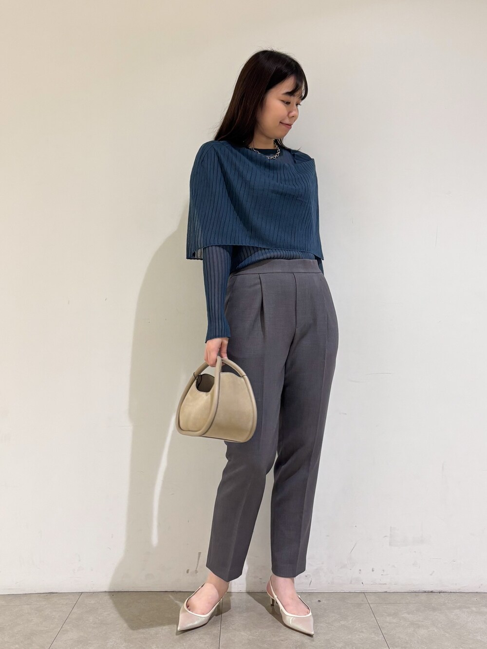 ブルー系のニット/セーター、グレー系のスラックスを着用したレディースの秋コーディネートの2枚目の写真