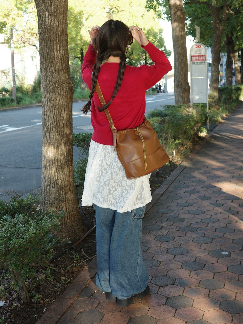 レッド系のカーディガン/ボレロ、ブラウン系のショルダーバッグ、ブルー系のデニムパンツを着用したレディースの秋コーディネートの2枚目の写真