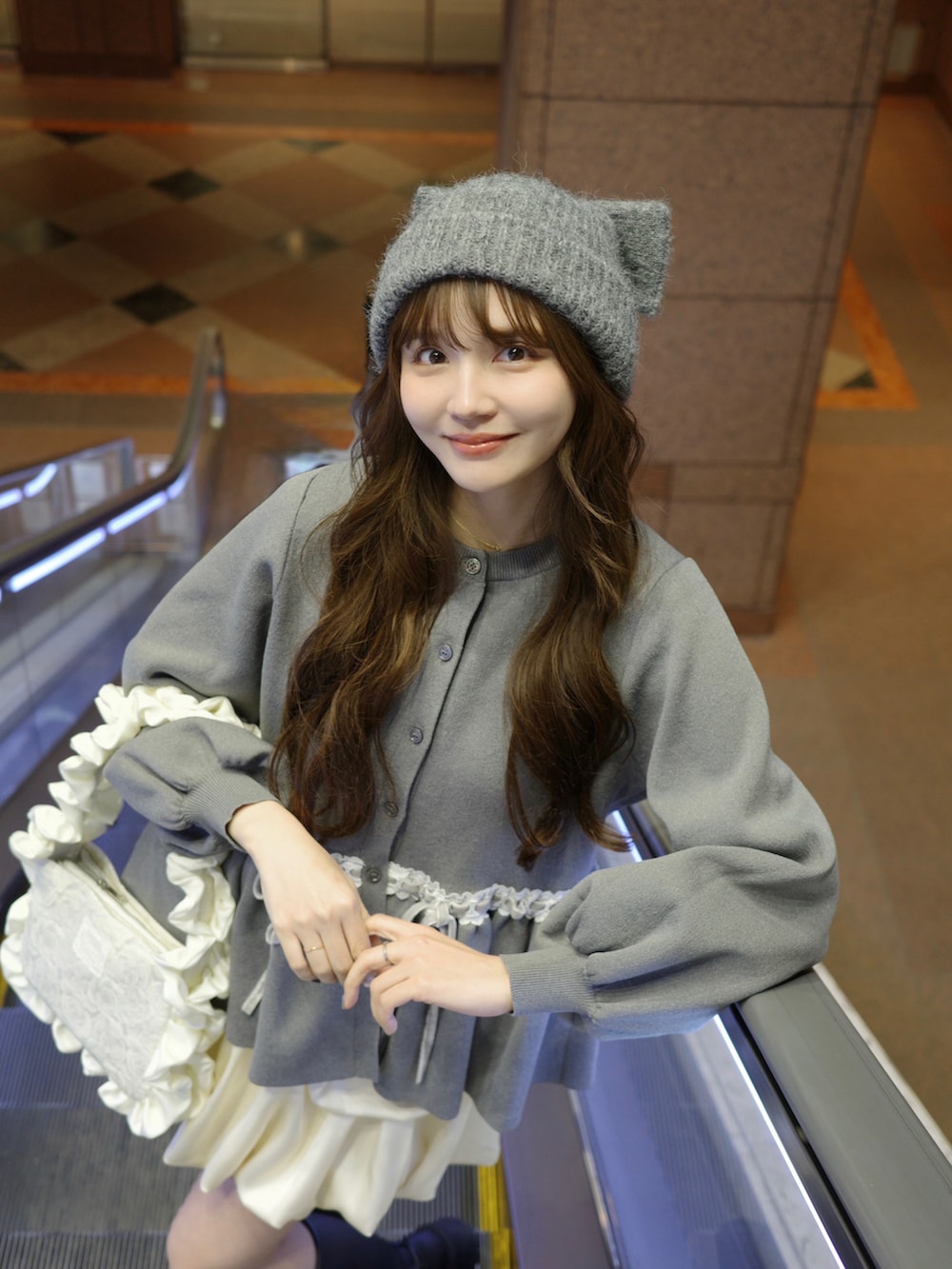 グレー系のカーディガン/ボレロ、ホワイト系のハンドバッグ、グレー系のニットキャップ/ビーニーを着用したレディースの冬コーディネートの2枚目の写真