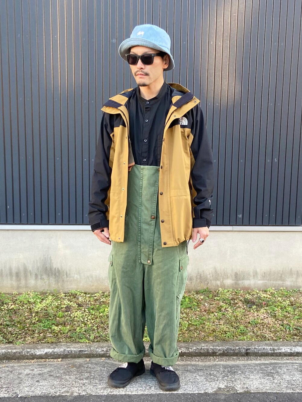 ブラウン系のジャケット/アウター、ブラック系のシャツ/ブラウス、グリーン系のサロペット/オーバーオールを着用したメンズの秋コーディネートの3枚目の写真