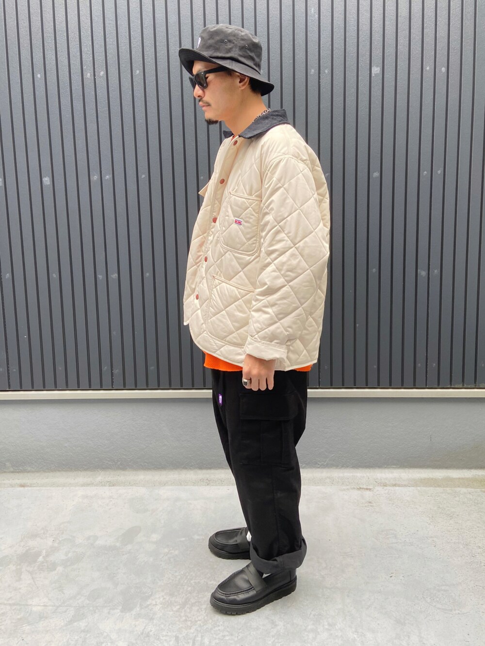 ホワイト系のカバーオール、オレンジ系のTシャツ/カットソー、ブラック系のカーゴパンツを着用したメンズの冬コーディネートの2枚目の写真