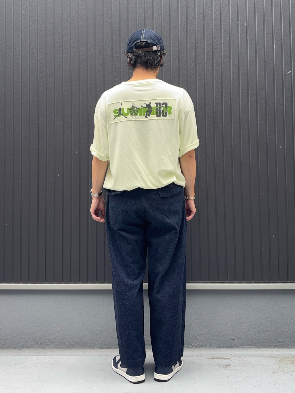 イエロー系のTシャツ/カットソー、ブルー系のデニムパンツ、グレー系のスニーカーを着用したメンズの秋コーディネートの3枚目の写真