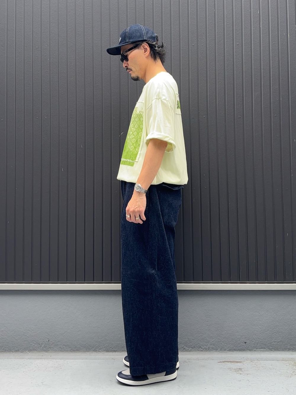 イエロー系のTシャツ/カットソー、ブルー系のデニムパンツ、グレー系のスニーカーを着用したメンズの秋コーディネートの2枚目の写真