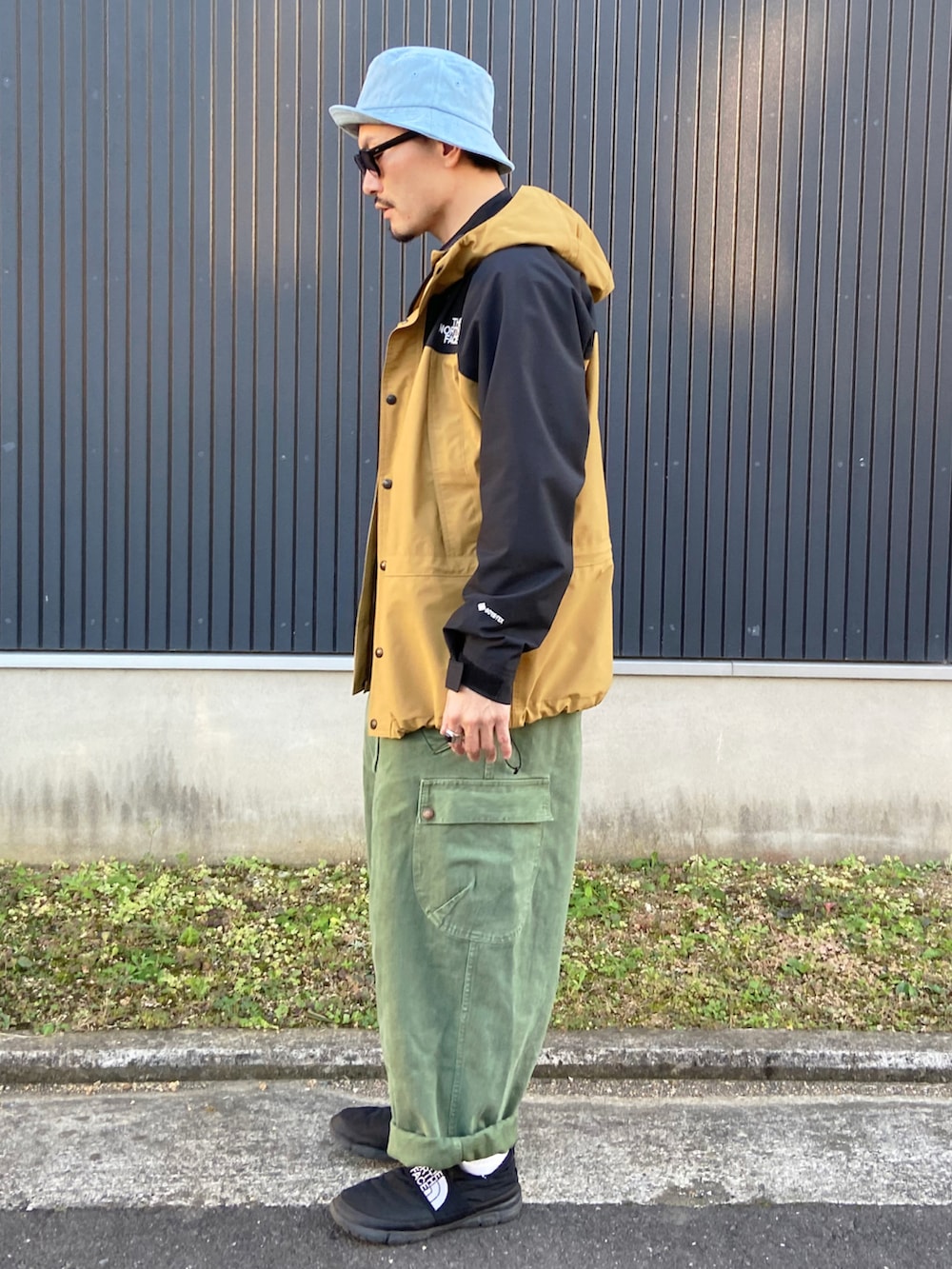 ブラウン系のジャケット/アウター、ブラック系のシャツ/ブラウス、グリーン系のサロペット/オーバーオールを着用したメンズの秋コーディネートの2枚目の写真
